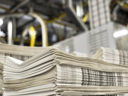 stack of freshly printed daily newspapers transported to a printing plant, in the background machines and technical equipment of a large printing plant