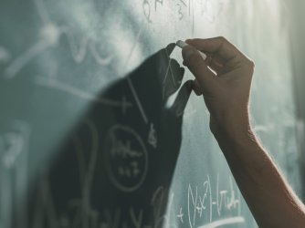 Professor writing mathematical formulas on the chalkboard, hand close up