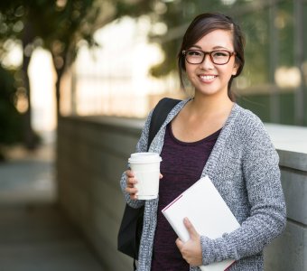 university student smiling with coffee and book bag on campus