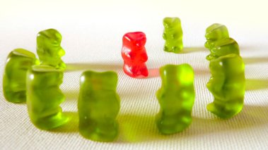 A group of green gummy bears surrounding a red gummy bear in a threatening manner.