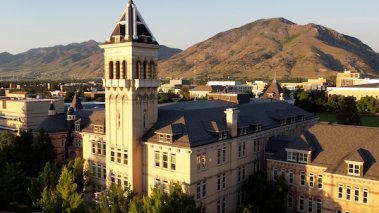 Utah State University Old Main Building at sunset with mountains.