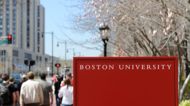 People walking past a red 'Boston University' sign.