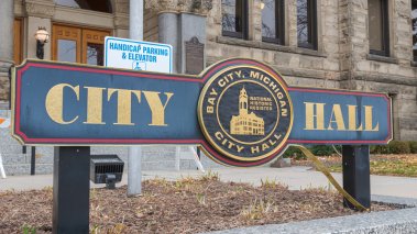 Wide angle close up of City Hall sign in Downtown Bay City, Michigan. The sign is in the foreground with the City Hall clock tower in the background.