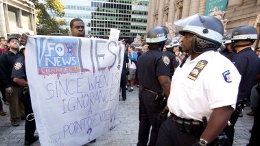 A policeman walks by a protester who is holding a sign that reads 'Fox News Lies' on the 1yr anniversary of the Occupy Wall St protests on September 17, 2012 in New York City