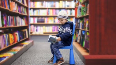 small boy reading a book in a library