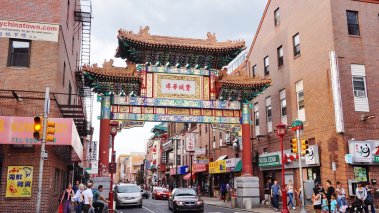 Friendship Gate in Philadelphia's Chinatown with cars and pedestrians passing beneath.