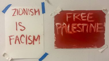Two paper signs posted on a door, one reading "Free Palestine" and the other "Zionism is Fascism"