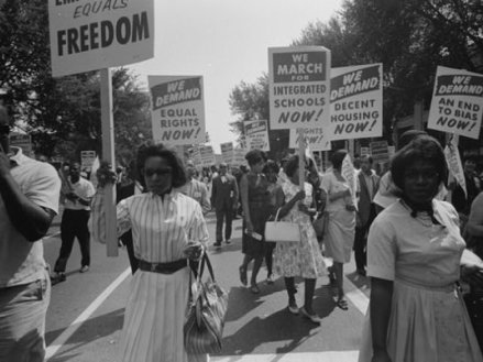 Photo of African American women at the March on Washington on 28 August 1963 carrying signs for equal rights, integrated schools, decent housing, and an end to bias.