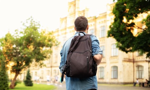 Student university standing with his back to the camera and his backpack on one shoulder and walking in university campus