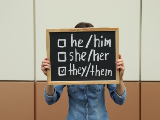 Woman holding chalkboard with list of gender pronouns near wall.jpg