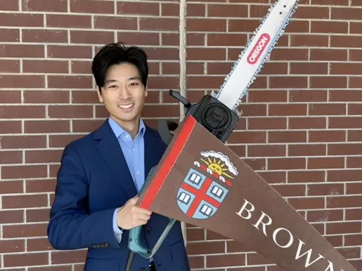 Alex Shieh holding a chainsaw and a Brown University pennant