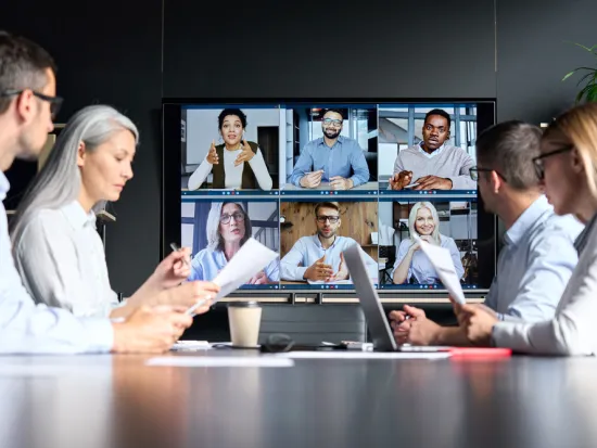 Global corporation online videoconference in meeting room with diverse people sitting in modern office and multicultural multiethnic colleagues on big screen monitor
