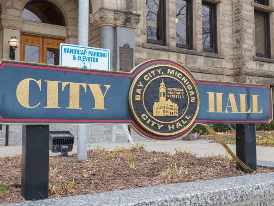 Wide angle close up of City Hall sign in Downtown Bay City, Michigan. The sign is in the foreground with the City Hall clock tower in the background.