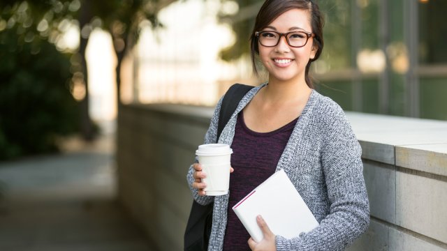 university student smiling with coffee and book bag on campus