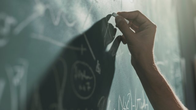 Professor writing mathematical formulas on the chalkboard, hand close up