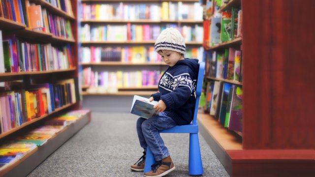 small boy reading a book in a library