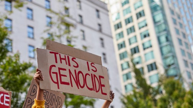 Women holding sign "this is genocide" written in red marker