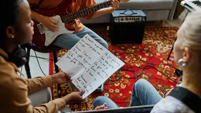 Close up of black young woman writing songs with music band and holding lyrics sheet
